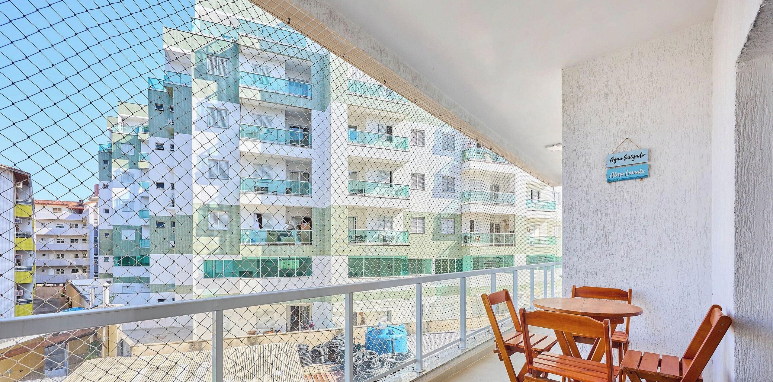 A balcony with a view of multi-story buildings, a table with chairs, and a sign on the wall.