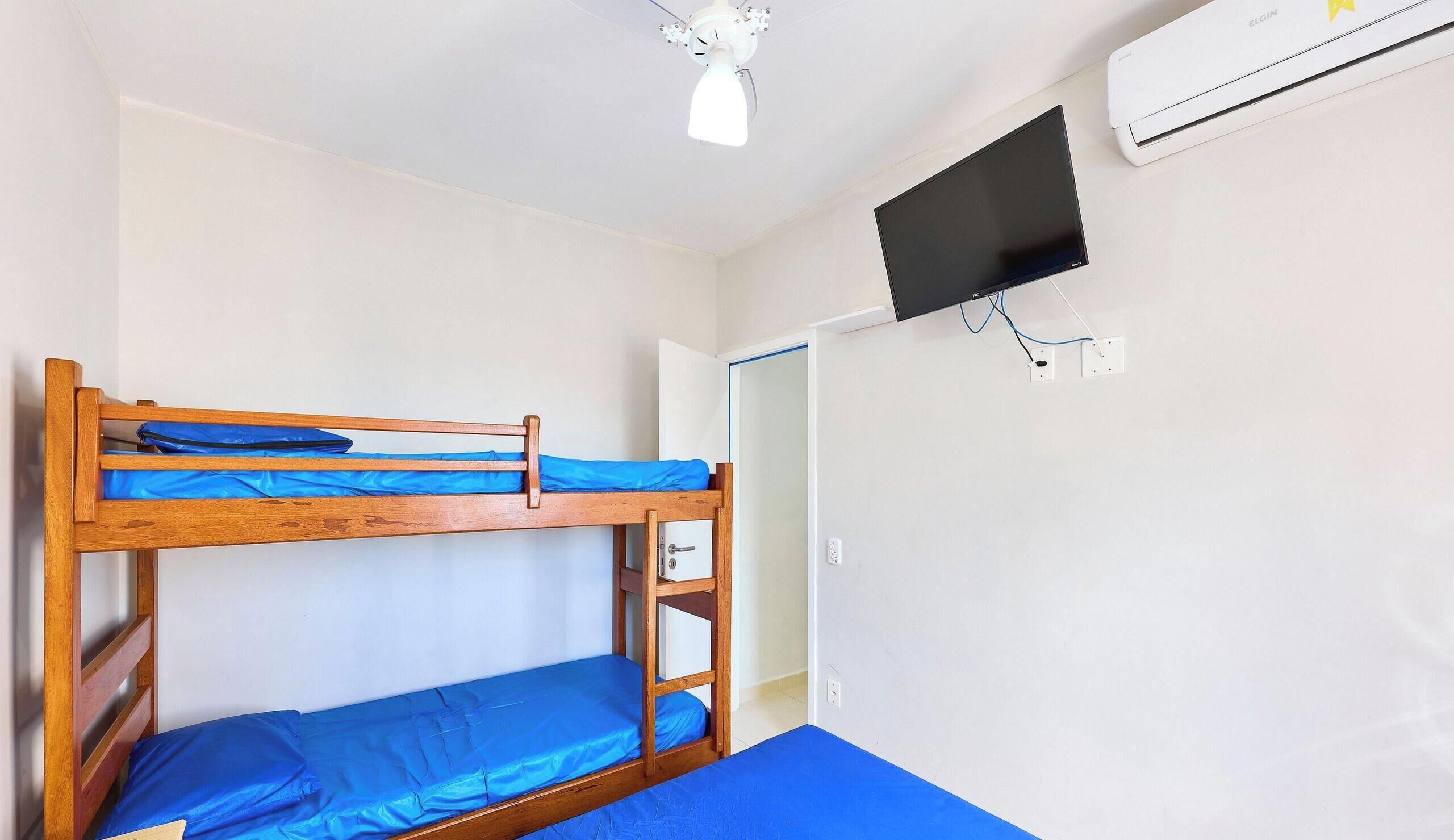 A bunk bed room with a ceiling fan, an air conditioning unit, and a television mounted on the wall.