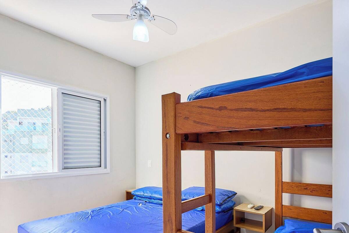 A bunk bed room with a ceiling fan, a window with blinds, and a small bedside table with a lamp.