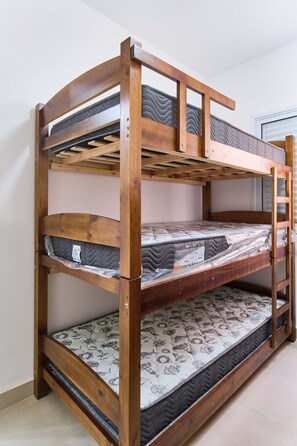 Ein Etagenbett mit drei Schlafstellen, Holzrahmen und gemusterten Matratzenauflagen.