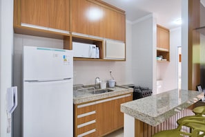 A kitchen with wooden cabinets, a white refrigerator, a granite countertop, and a sink. - Residencial Saint Barth (Ubatuba)
