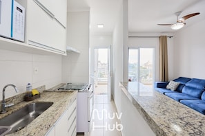 A modern kitchen with a granite countertop, stainless steel sink, and a built-in oven. - Residencial Saint Barth (Ubatuba)