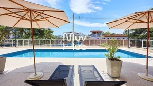 A rooftop pool area with two sun umbrellas, a glass table, and a potted plant. - Residencial Saint Barth (Ubatuba)