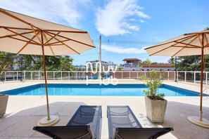 A rooftop pool area with two sun umbrellas, a glass table, and a potted plant. - Residencial Saint Barth (Ubatuba)