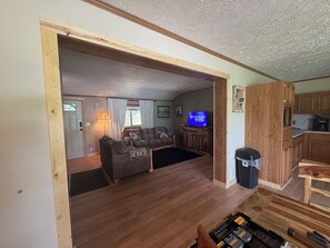 Una sala de estar con televisor, armarios de madera y una zona de cocina.