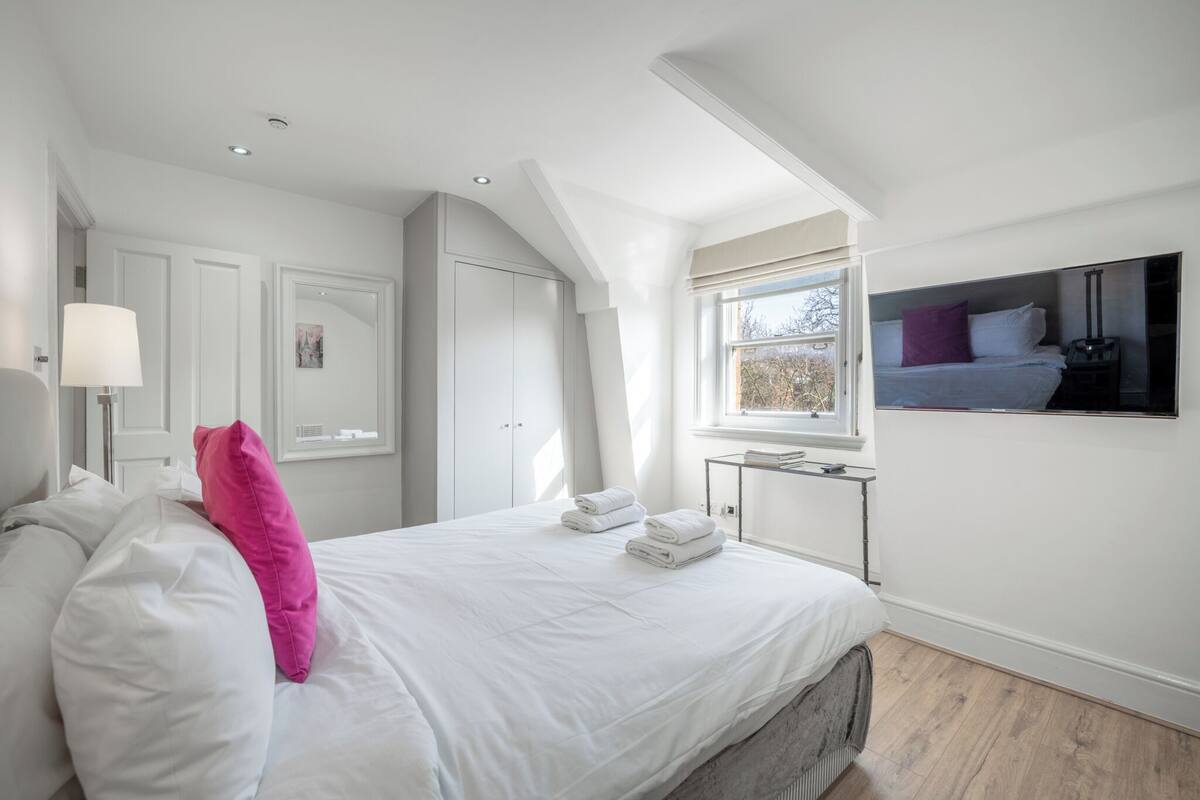 A modern bedroom with a large bed, a window with a view, a TV, and a wardrobe.
