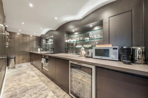 A modern kitchen with a built-in microwave, coffee maker, and glass display shelves. - The Knightsbridge Residences (London)