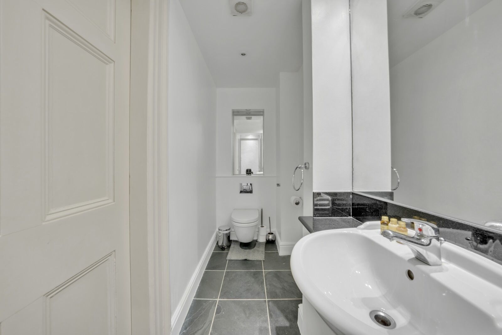 Een moderne badkamer met een wit toilet, een bidet, een wastafel met spiegel en een bad.