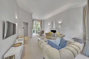 A spacious living room with a sofa, a television, and a fireplace. - The Knightsbridge Residences (London)