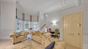 A spacious living room with a high ceiling and a staircase leading to an upper floor. There is a dining area with a table and chairs visible in the background. - The Knightsbridge Residences (London)