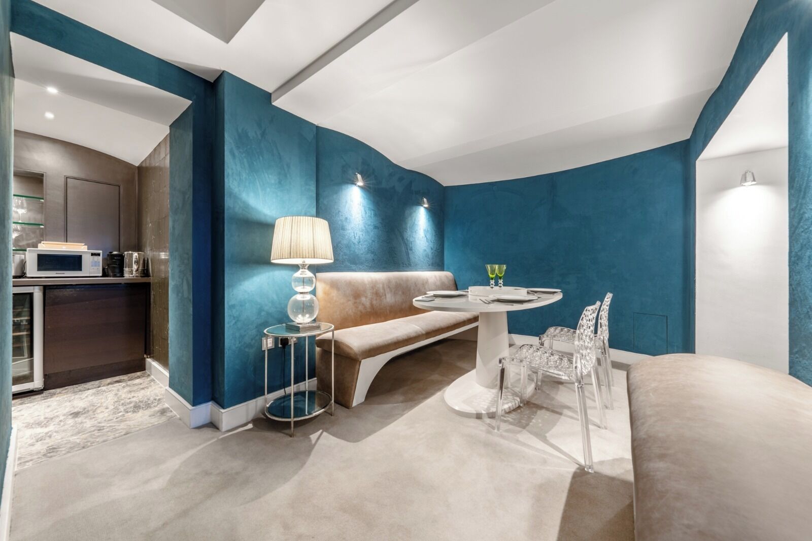 Uma sala de estar moderna com uma parede azul decorativa, uma mesa de jantar redonda com cadeiras, um sofá e uma luminária.