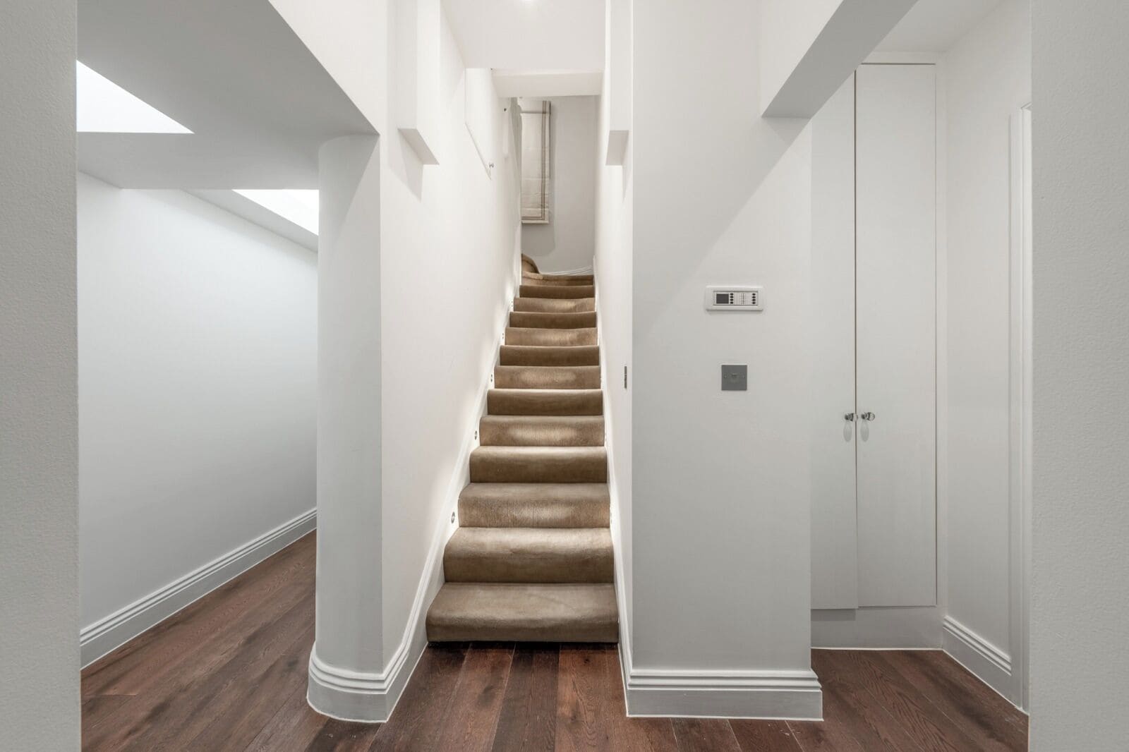 Un interior moderno con una escalera alfombrada, paredes blancas y suelo de madera.