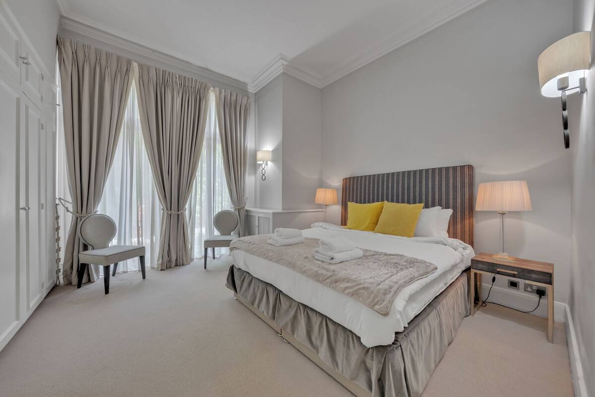 A modern hotel room with a large bed, two bedside tables with lamps, a chair, and a desk.