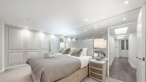 A modern bedroom with a large bed, bedside tables, a mirror, and a walk-in closet. - The Knightsbridge Residences (London)