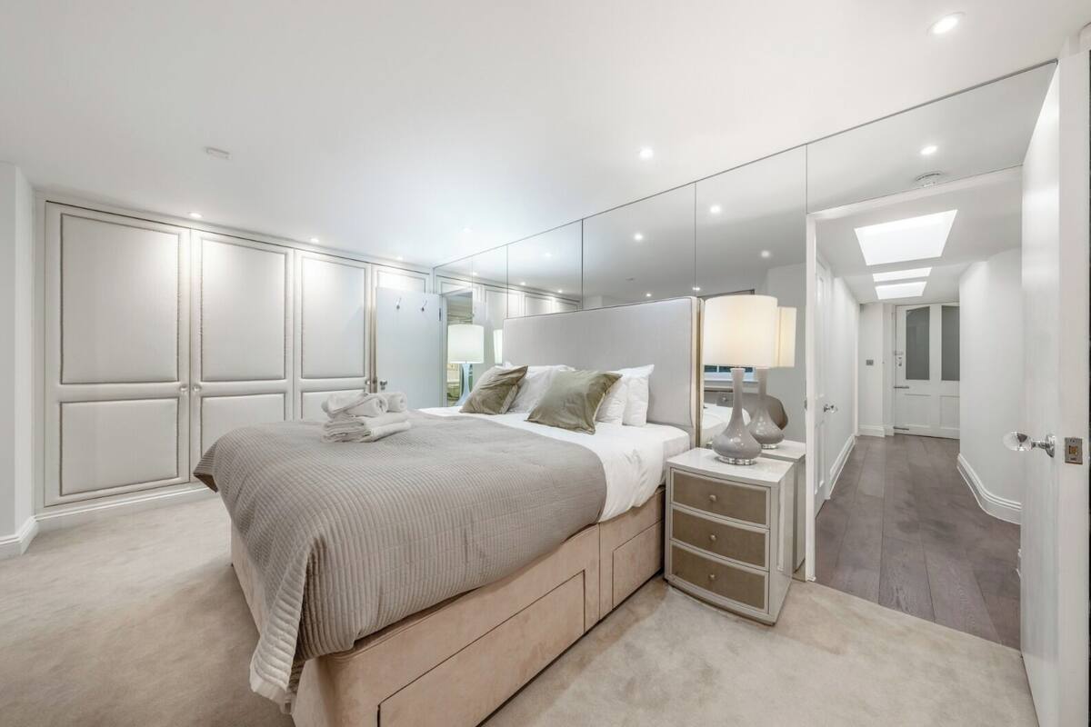 A modern bedroom with a large bed, bedside tables, a mirror, and a walk-in closet.