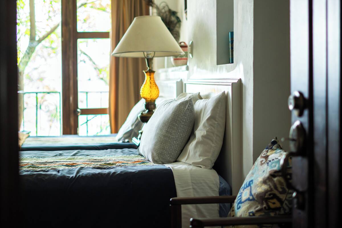 Un dormitorio con cama, lámpara y ventana con cortinas.