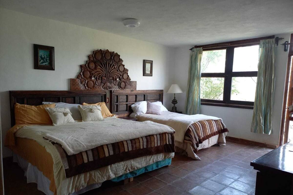 Habitación con dos camas, cabecera de madera, ventana con cortinas y una lámpara.