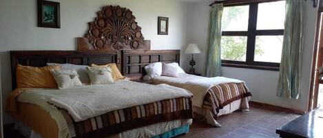 Habitación con dos camas, cabecera de madera, ventana con cortinas y una lámpara.