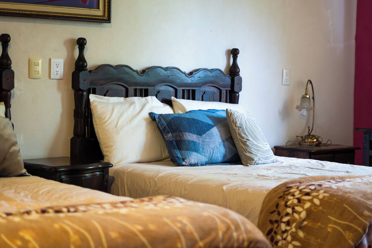 Una cama doble con cabecera de madera, dos mesitas de noche y una mesita auxiliar con lámpara.