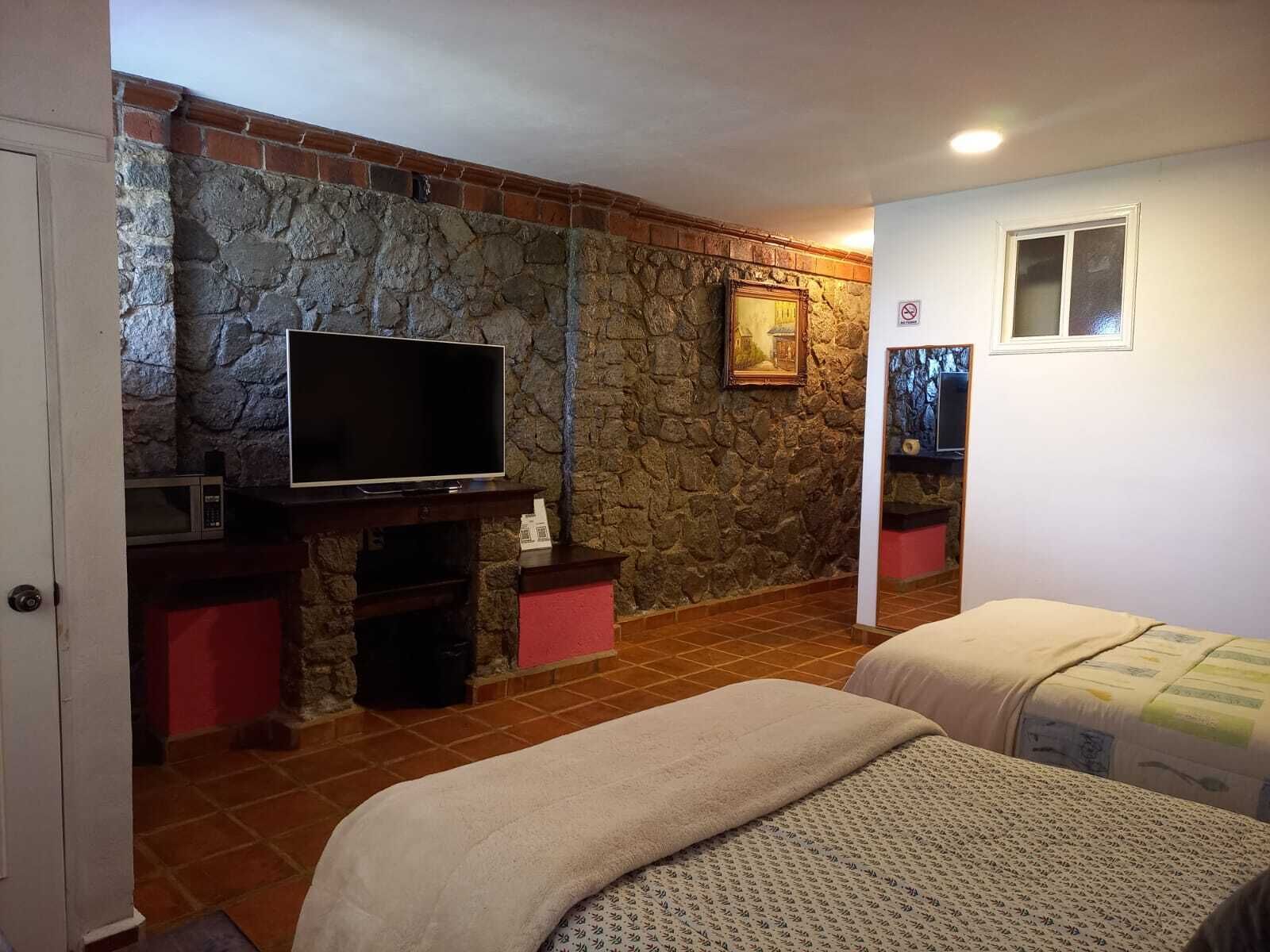 Un dormitorio con pared de piedra, televisor, cama y una ventana pequeña.