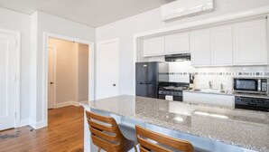 Eine moderne Küche mit weißen Schränken, einer Granit-Arbeitsplatte, einem Edelstahl-Kühlschrank, einem Herd und einer Mikrowelle.
