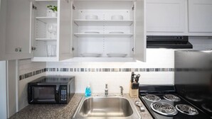 Una cocina con armarios blancos, un lavamanos de acero inoxidable, un microondas, una estufa y un salpicadero de azulejos.