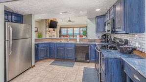 A modern kitchen with blue cabinets, stainless steel appliances, and a large window offering a view.