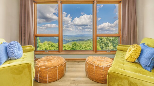 A room with a large window, two yellow sofas, and two brown ottomans.