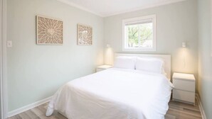 Une chambre à coucher comprenant un lit, deux tables de chevet, une fenêtre et deux œuvres d’art murales.