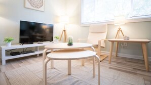 Un salon moderne doté d’un téléviseur à écran plat, de deux tables rondes, d’un canapé et d’une fenêtre avec des stores.