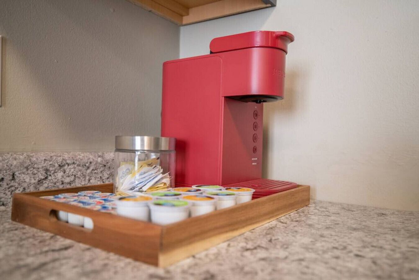 Een rode koffiemachine op een aanrecht met een bak kleurrijke koffiekapsules en een glazen pot.