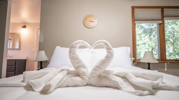 Ein Hotelzimmer mit einem Bett, einer Wanduhr und einem Fenster mit Blick auf Bäume.