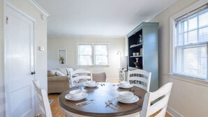 Ein Esszimmer mit einem runden Tisch, gedeckt für vier Personen, weißen Stühlen, einem Bücherregal und einem Fenster mit Jalousien.