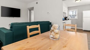 Una sala de estar moderna con un sofá verde, sillas de madera, una mesa de comedor de madera y un florero de vidrio con adornos.
