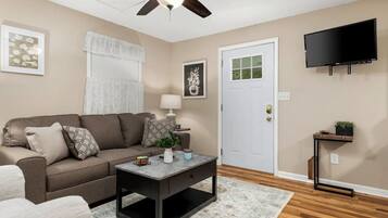 A living room with a brown sofa, a coffee table, a lamp, a TV, and a door.