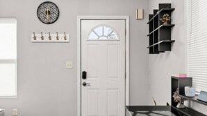 A hallway with a white door, a coat rack with hooks, a wall clock, and a black shelving unit with decorative items.