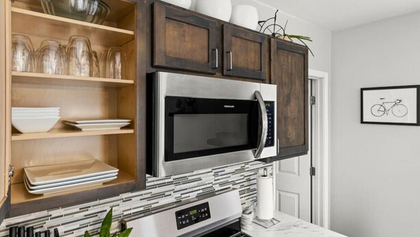 A kitchen with dark wooden cabinets, a stainless steel microwave, and a tiled backsplash.