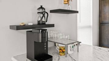 A modern kitchen with a coffee maker, glass mugs, and a coffee pot on shelves.
