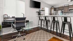 A modern kitchen with a flat-screen TV, bar stools, and a coffee machine.