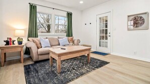 Een moderne woonkamer met een beige bank, een houten salontafel en een zwart vloerkleed.