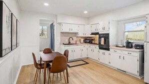 Een moderne keuken met witte kasten, een eettafel met stoelen en een raam dat voor natuurlijk licht zorgt.