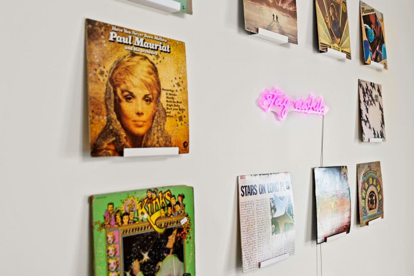 Paredes com diversas obras de arte, incluindo um letreiro de neon, uma capa de revista e várias peças emolduradas.