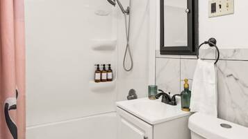 Een badkamer met een bad, toilet en wastafel. Er is een douche boven het bad en een handdoekrek is zichtbaar.