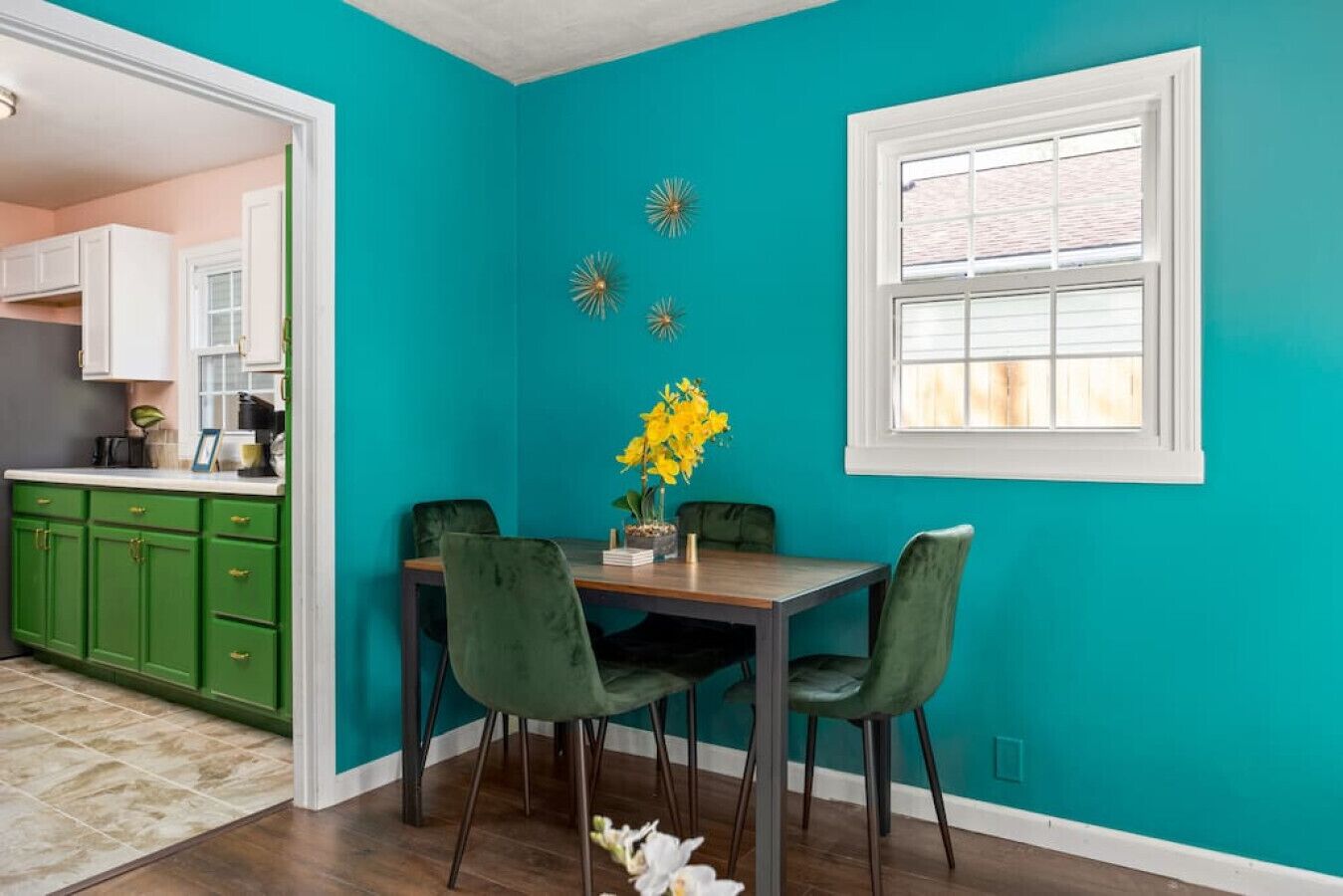 A dining area with teal walls, a wooden table, and green chairs.
