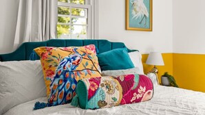 A bed with colorful pillows, a teal headboard, and a painting of a bird on the wall. - Art Deco Oasis: A Stylish Retreat (Peoria Heights)