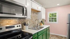 A modern kitchen with white cabinets, a stainless steel microwave, a black stove, and green cabinets. - Art Deco Oasis: A Stylish Retreat (Peoria Heights)