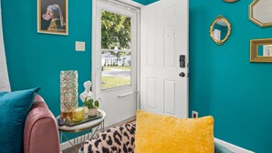 A teal-walled room with a white door, a framed picture, and a small table with a plant and a lamp. - Art Deco Oasis: A Stylish Retreat (Peoria Heights)
