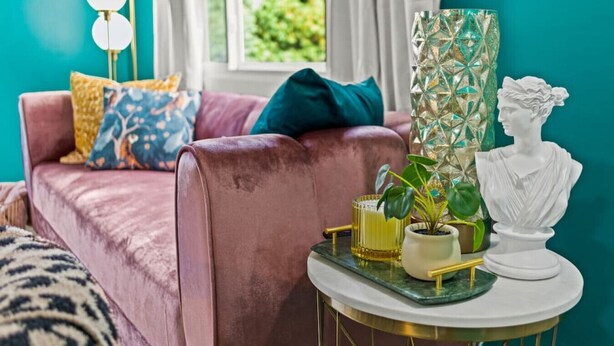A cozy living room with a pink sofa, decorative pillows, a green vase, a white bust, and a small table with a plant and a candle. - Art Deco Oasis: A Stylish Retreat (Peoria Heights)