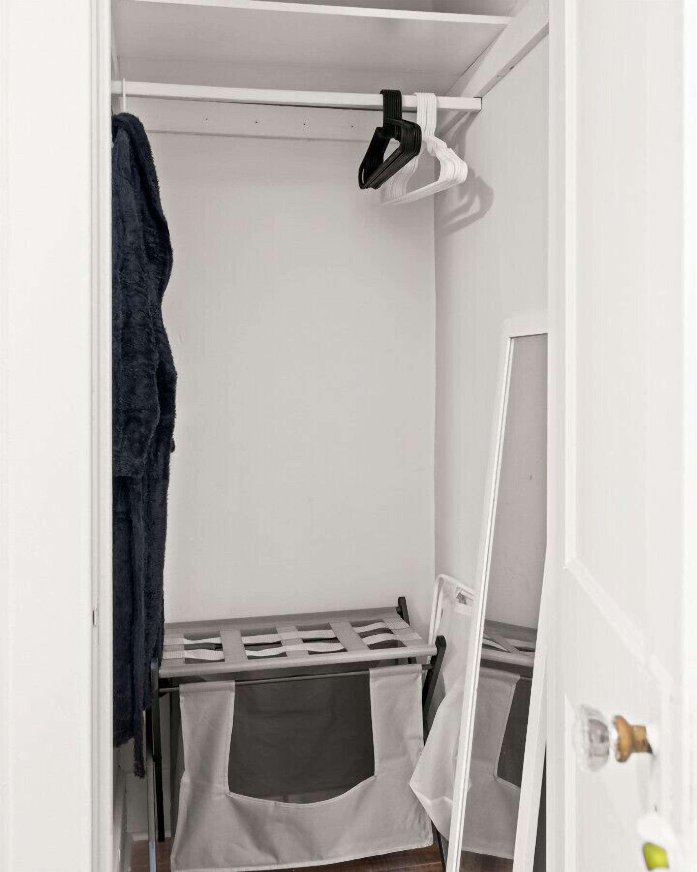 Een kleine, witte kast met een kledingroede, een spiegel en een bankje met opbergruimte.