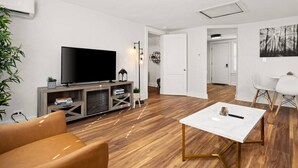 A modern living room with a flat-screen TV, wooden flooring, a white coffee table, and a seating area with a brown sofa.
